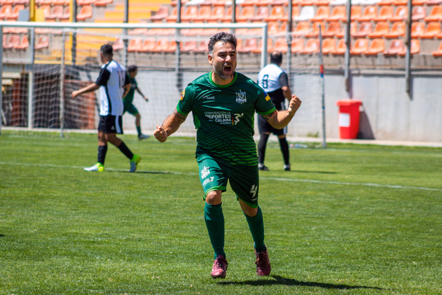 A player in green clenching his fists to celebrate a goal on the pitch