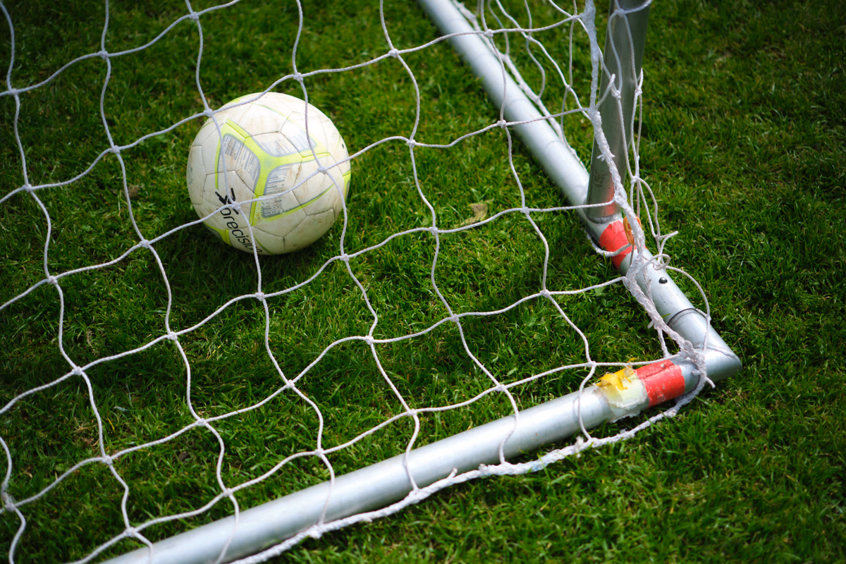 A football resting in the goal net on a grass pitch