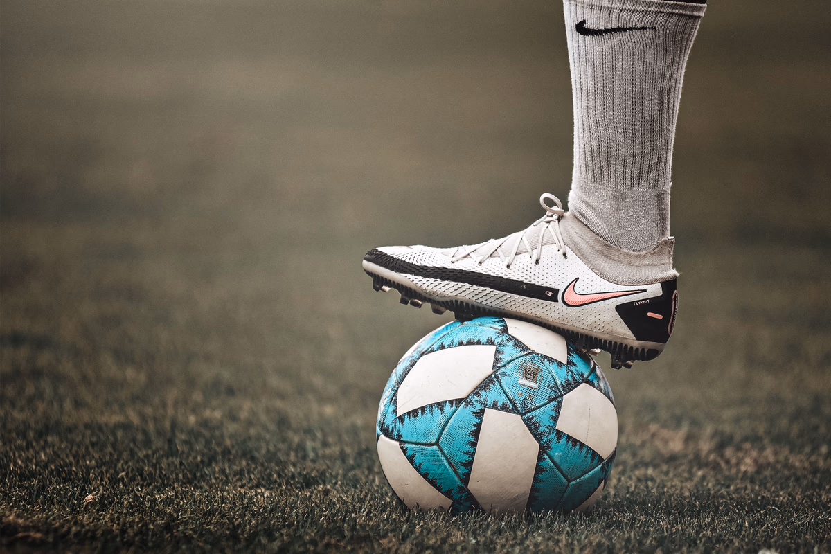 A close-up of a football boot resting on a ball on a grass pitch