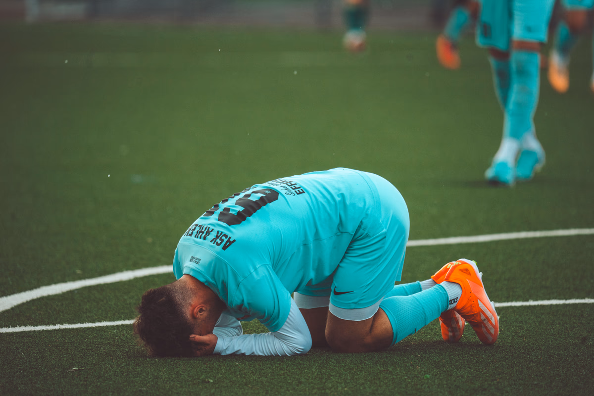 A footballer kneeling head-down in dejection on the pitch after a loss
