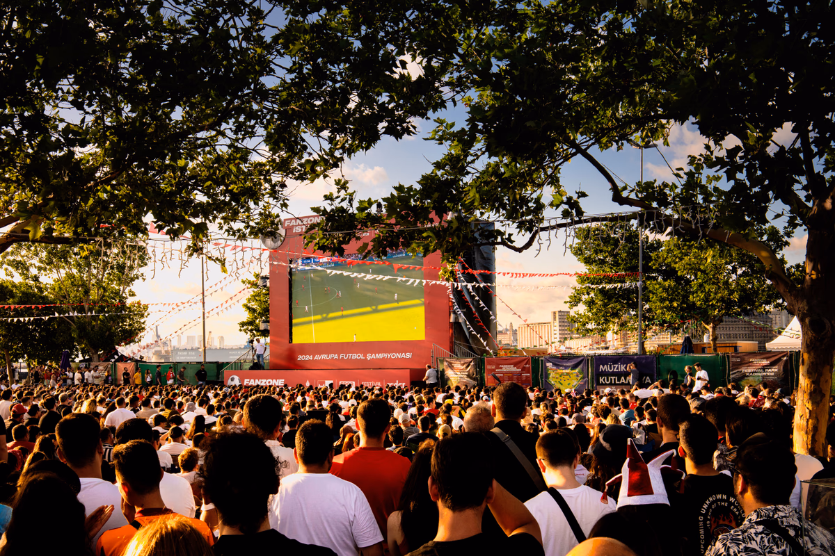 A crowd gathered to watch football on a big screen in a public park