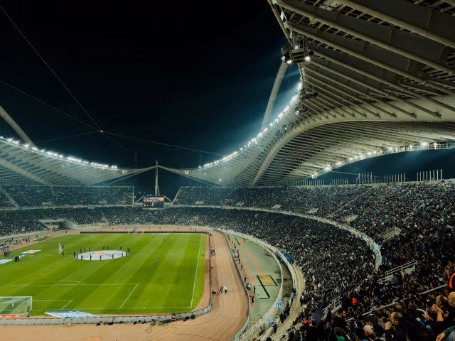 A full football stadium at night, floodlit during a match