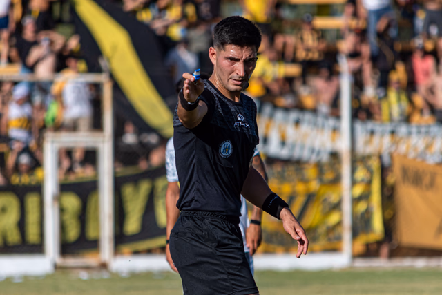A football referee in black signalling a decision during a match