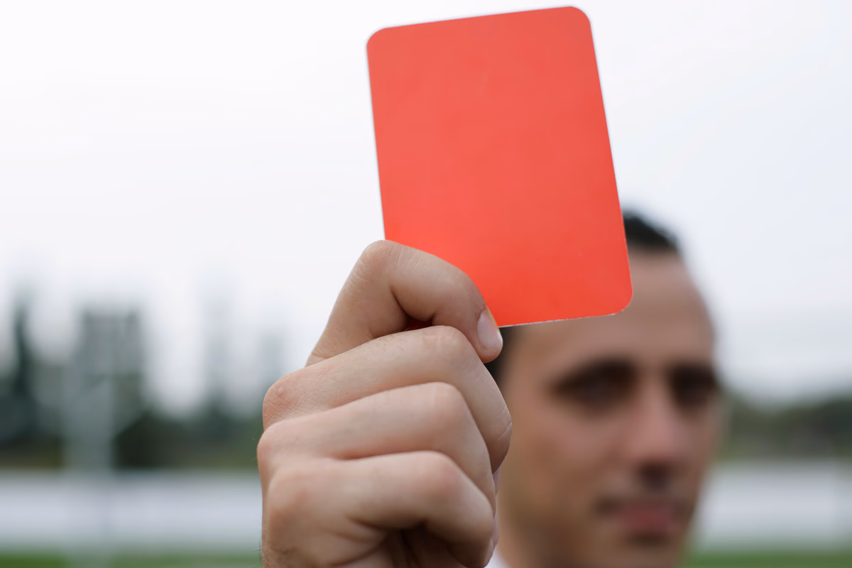 A referee holding up a red card on a football pitch